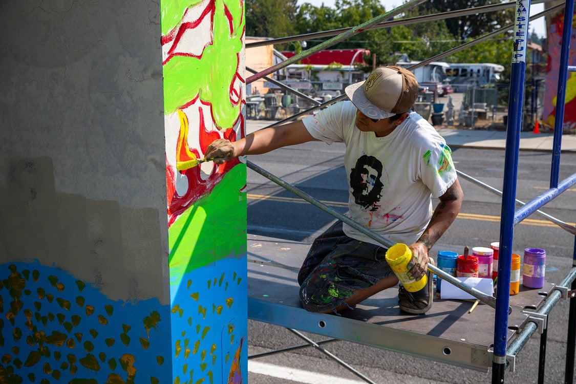 Local artist Rodolfo Redstone Serna paints a mural on the column of a bridge.