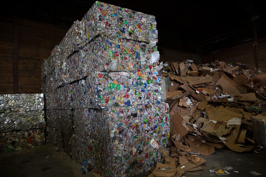 stacked bales of separated aluminum and tin stand next to a pile of lose cardboard