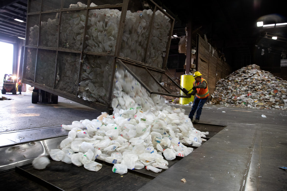 a worker opens a huge bin of plastic milk jugs onto a conveyor belt