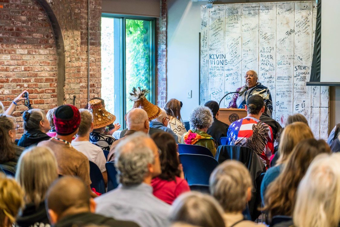 Woman speaks to seated crowd 