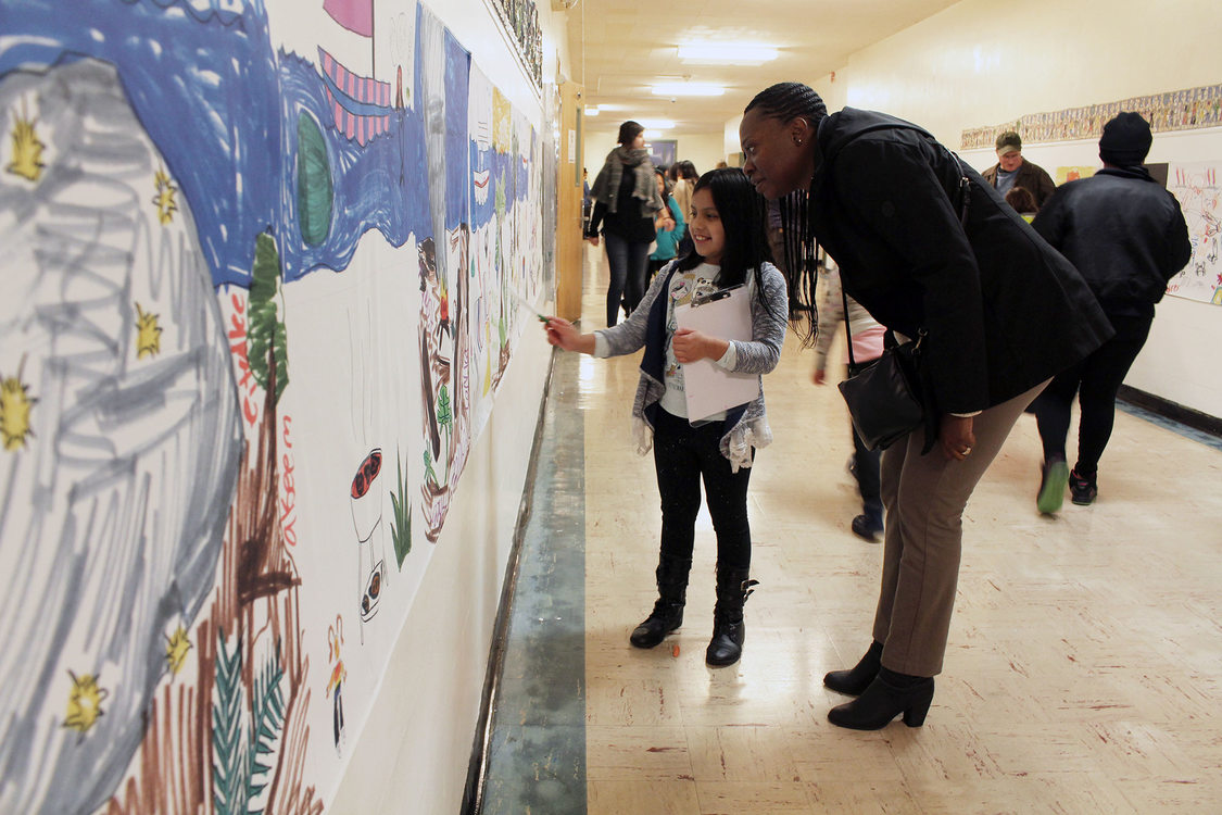 a little girl and a woman look at art work together in a school hallway
