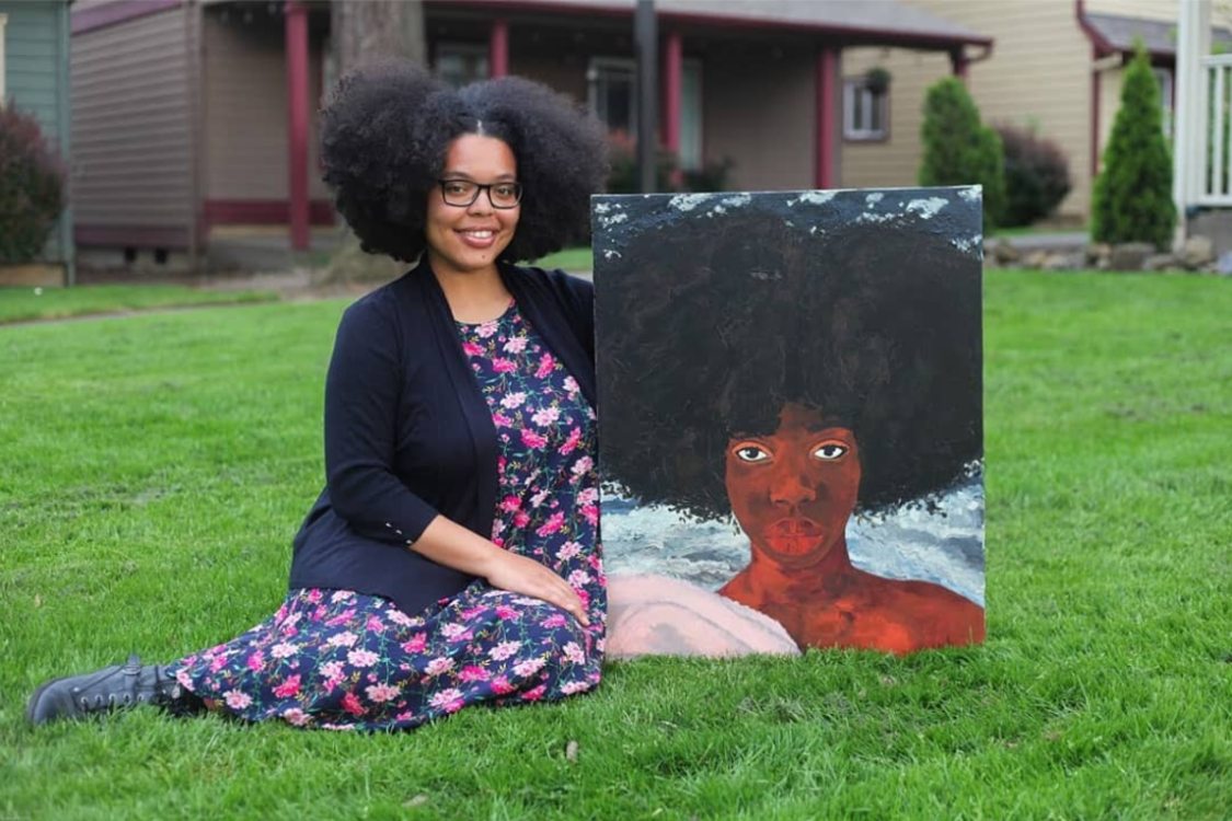  an artist sits on a grassy lawn while holding a painting she created