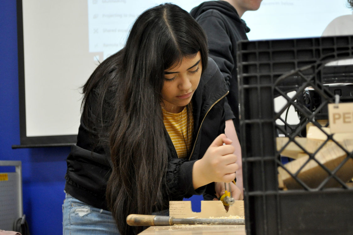 girl sawing a piece of wood in class