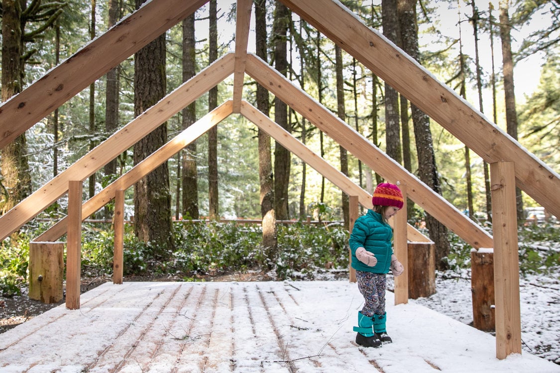 girl in winter clothes stand in nature play structure