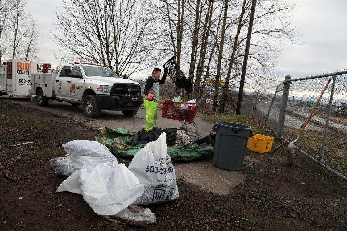 A man goes through dumped garbage on a bluff overlooking a highway