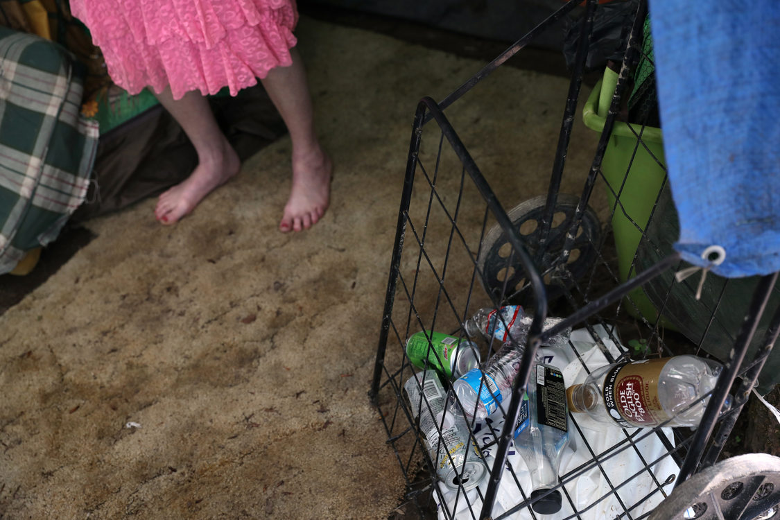 A woman stands next to an upright, metal cart filled with recyclables.