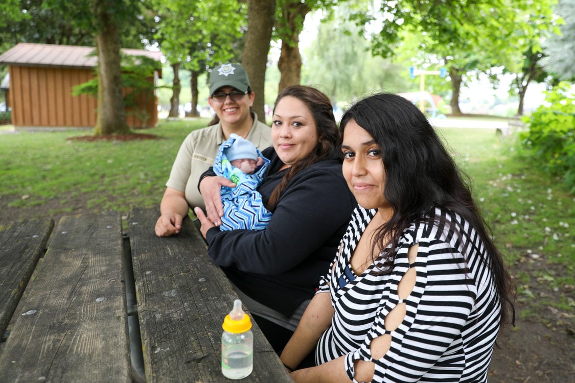 three woman sit together on bench in park with a baby