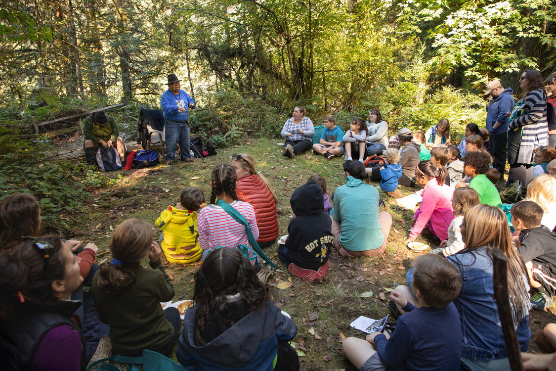 Ed Edmo shares traditions Indigenous stories to group sitting on the ground