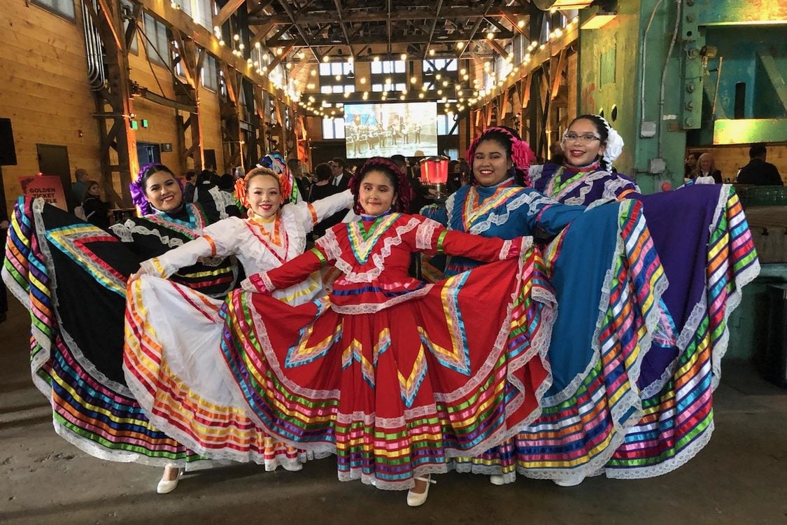 Five girls, members of a dance troupe, stand side to side as they fan out their brightly-colored skirts.