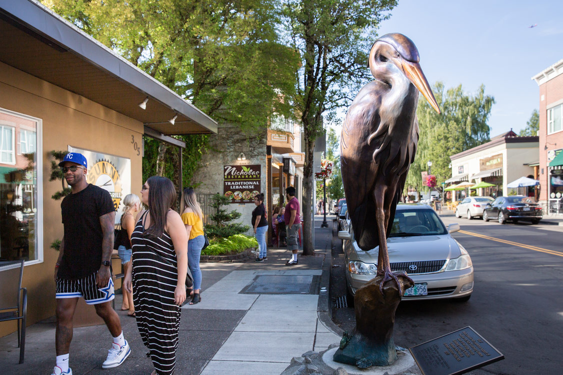 pedestrians and a sculpture of a heron on a sidewalk in downtown Gresham
