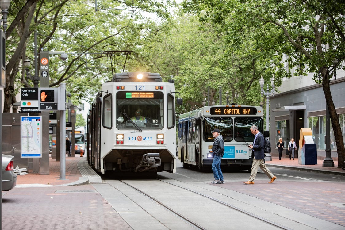 pedestrians cross in front of a MAX train and TriMet bus