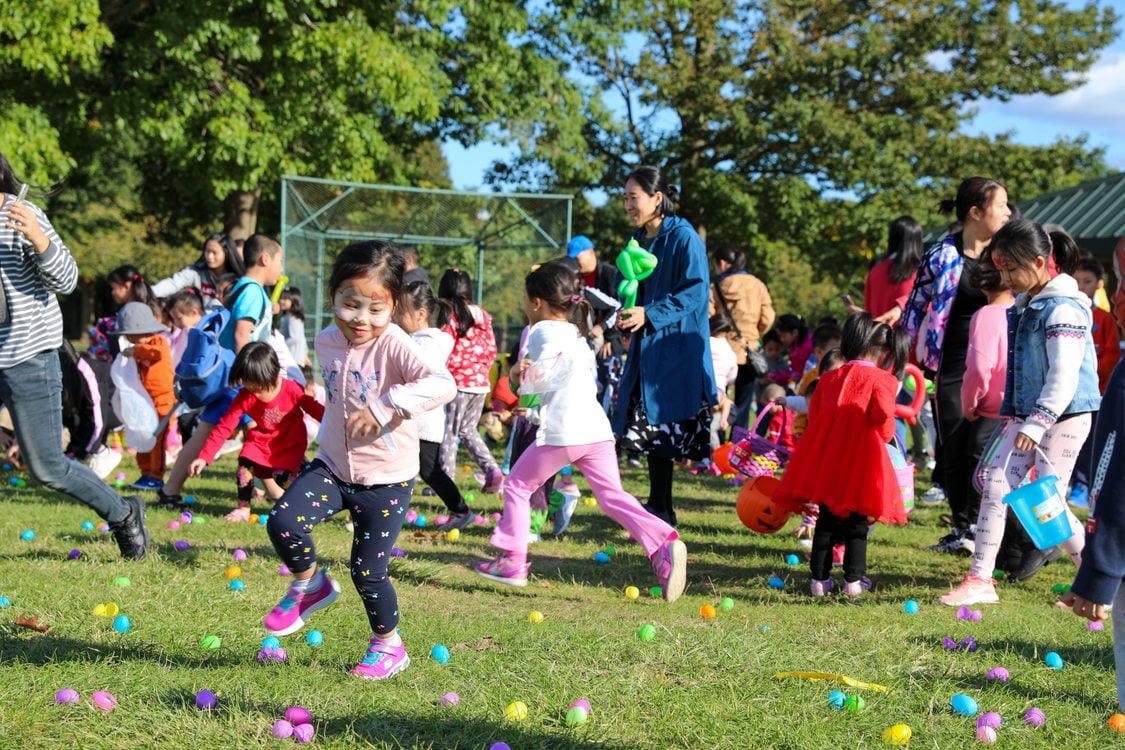 Children running around the field as they pick up plastic colored eggs at the park
