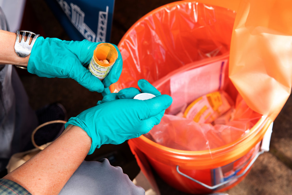 gloved hands open a prescription bottle to remove unused medications