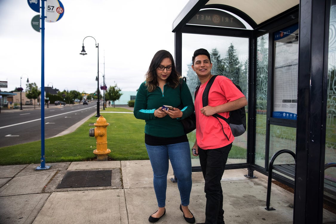 Two people, a young man and woman, wait at a bus stop.