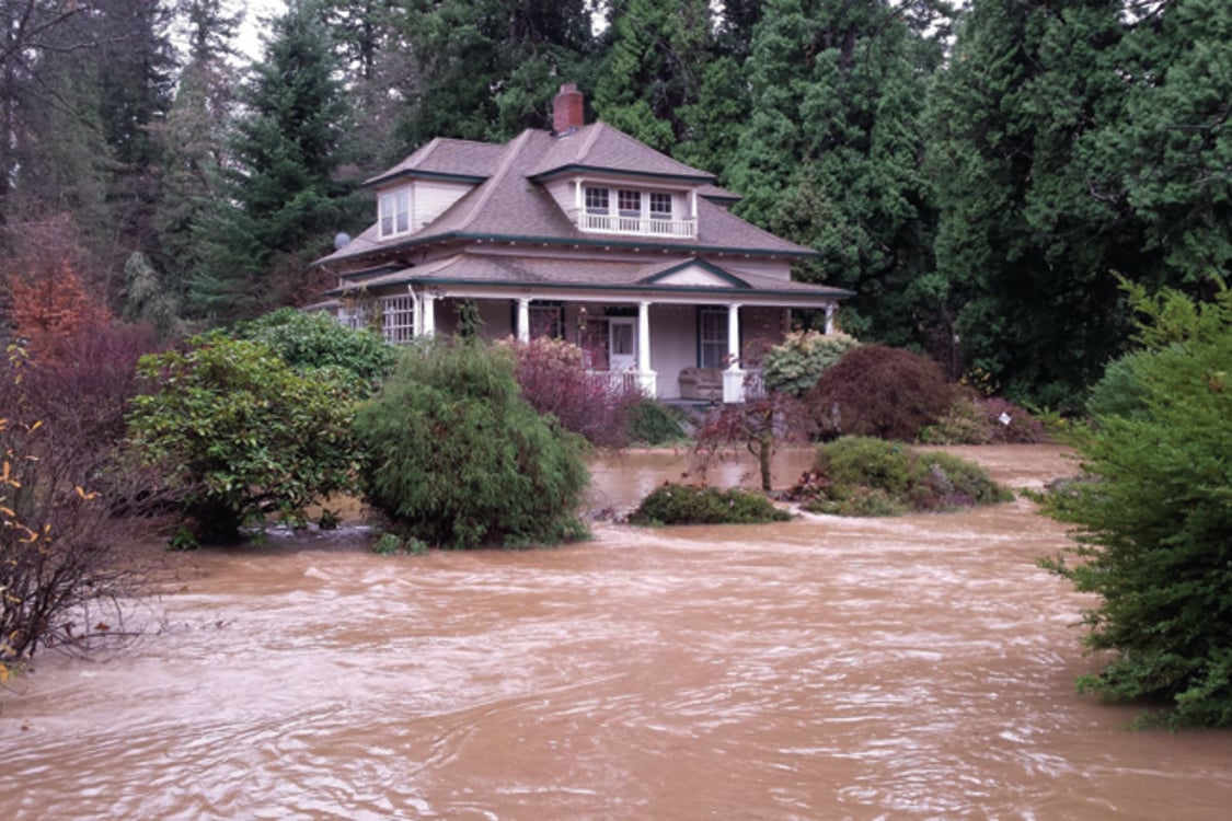 A large house is surrounded by muddy flood water.
