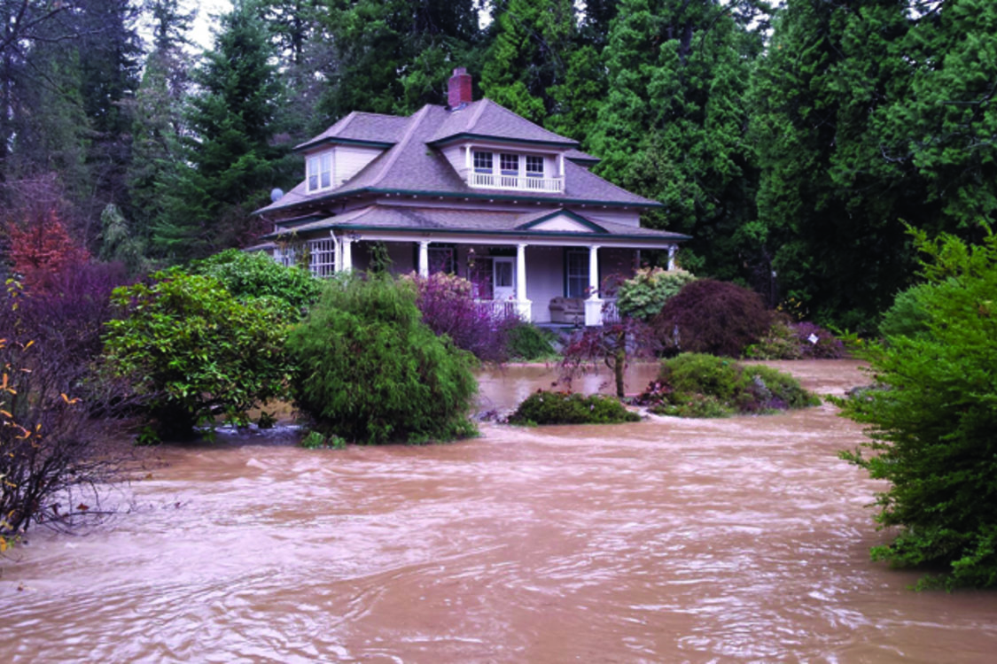 A large house is surrounded by muddy flood water.