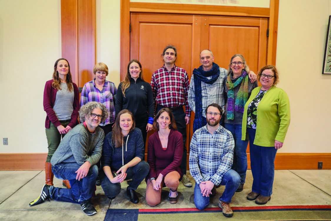 Two rows of people pose for a photograph. They are all wearing outdoors-type clothing, like flanel.