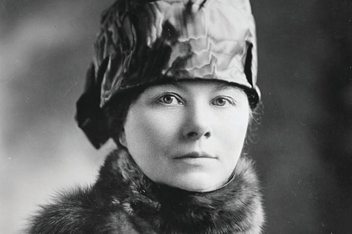 A white woman wearing a silk hat and fur scarf poses for a black-and-white portrait.