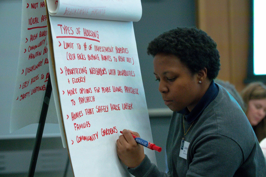 a young woman takes notes on a large easal pad during a community workshop