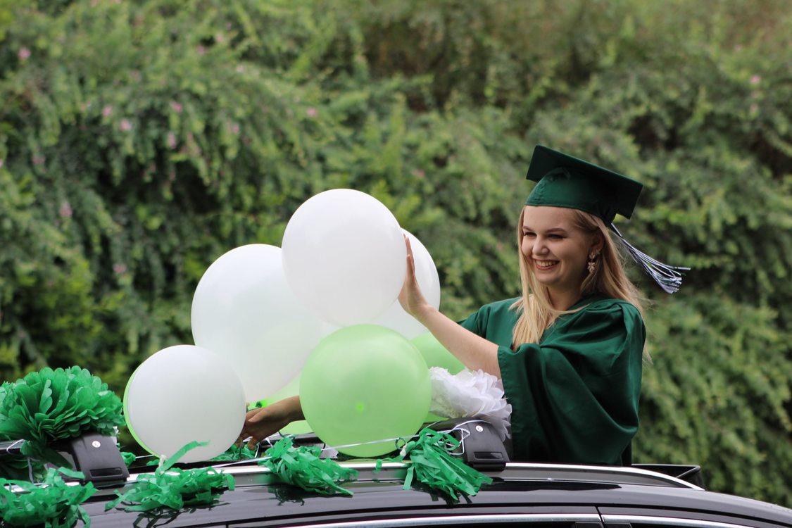 a high school student, standing through a car's sunroof, adjusts balloons as she waves for photos during a drive-thru graduation ceremony June 8 at Wilson High School.