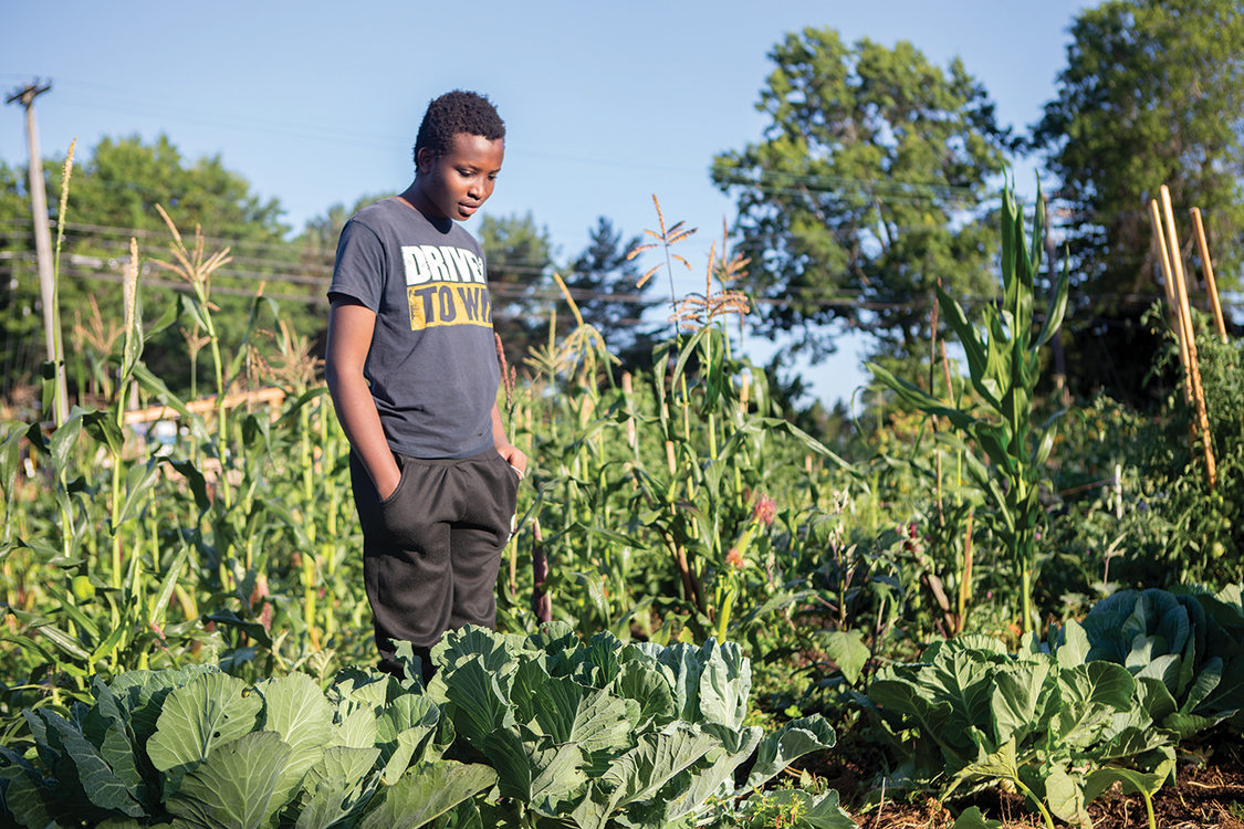 A young black man stands in a garden.