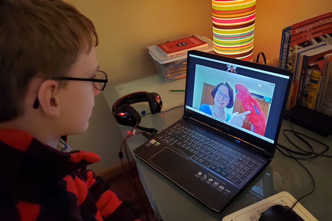 A young child attends an online distance learning program hosted by a Metro educator from his laptop on a desk at home