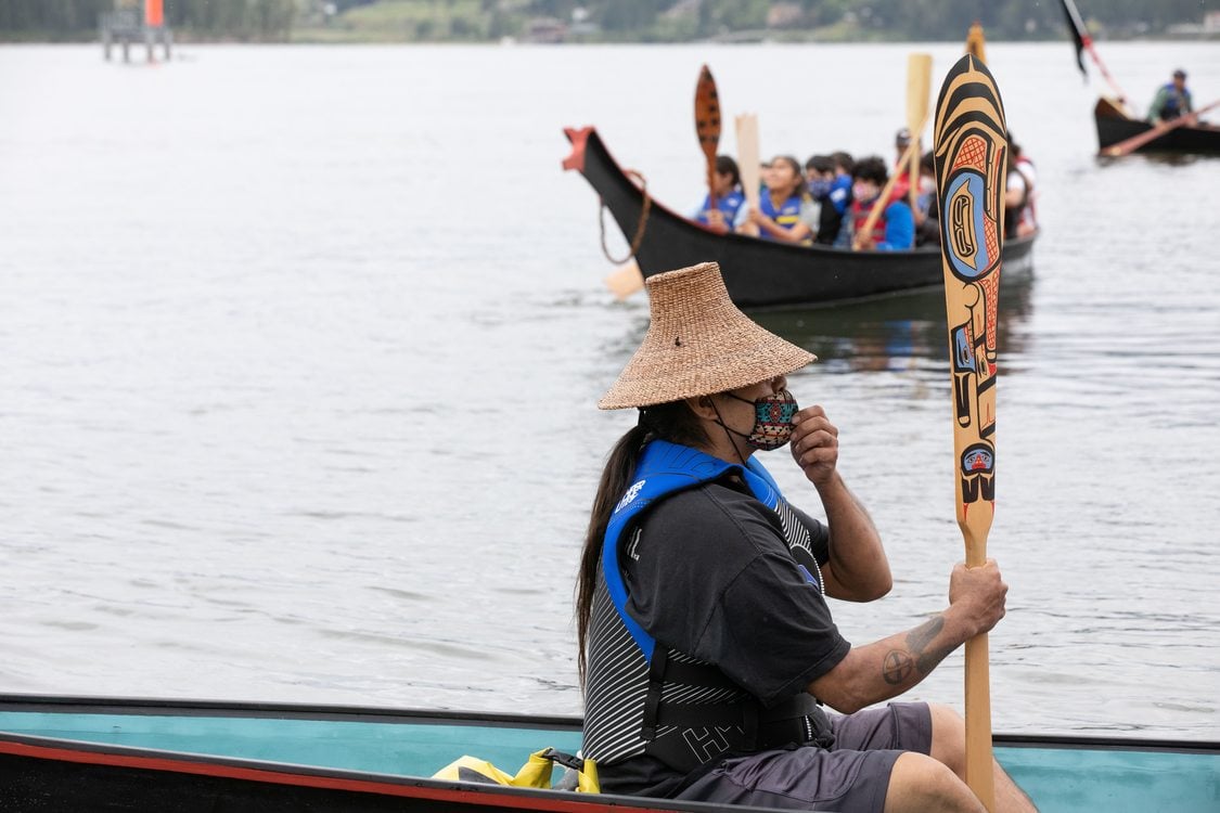 a person with a hat sits in a canoe holding a decorative oar in their hand