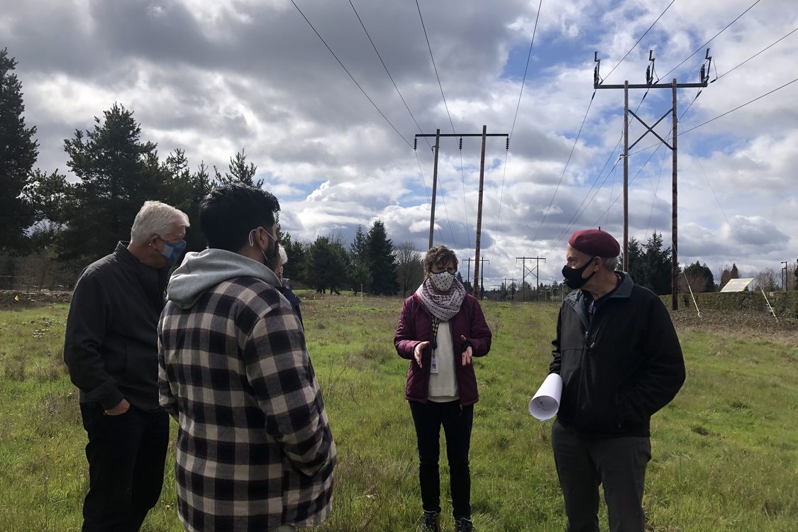 Metro Councilor Gerritt Rosenthal speaks with Metro staff in a grassy open field near the Westside Trail pedestrian bridge project on a partly cloudy spring day
