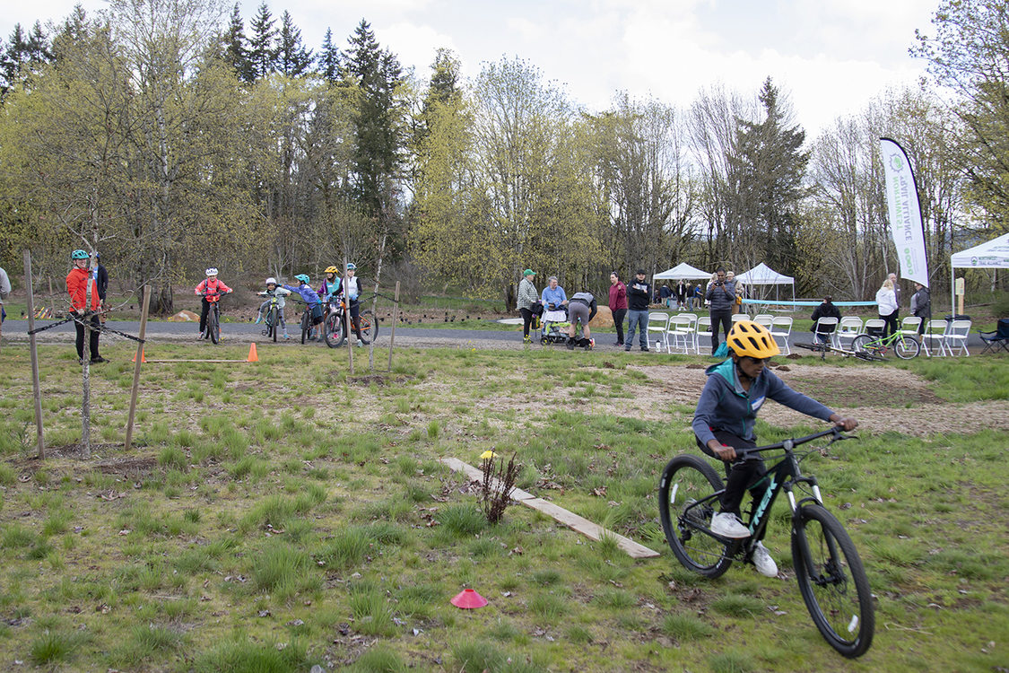 A young mountain biker rides along a grass lawn with small obstacles.