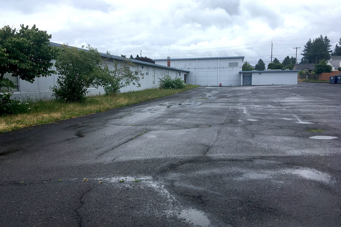 A bare, cracked field of asphalt behind a one-story school.