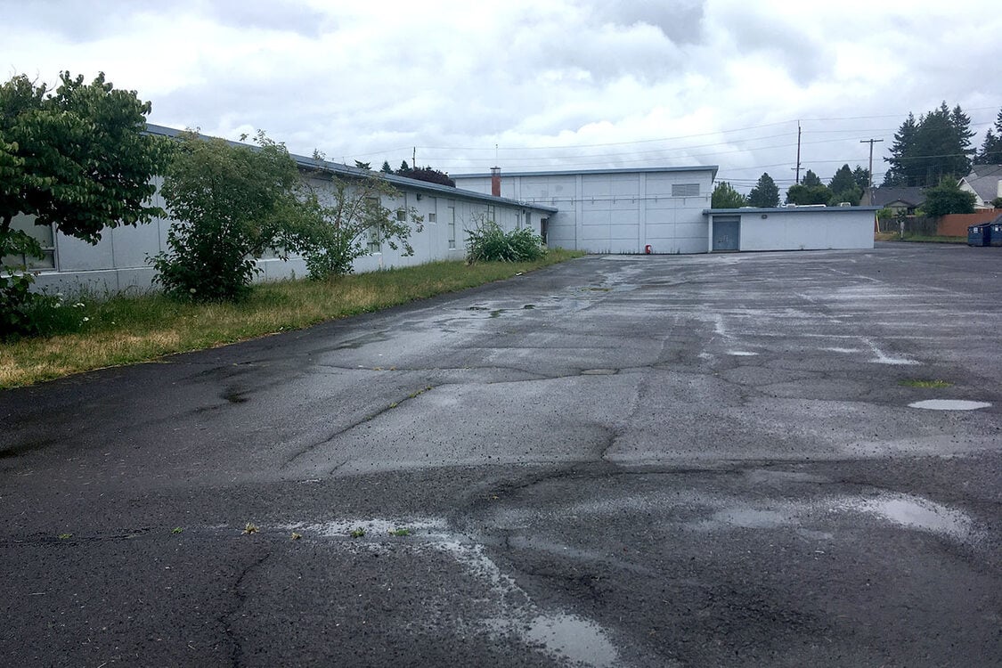 A bare, cracked field of asphalt behind a one-story school.