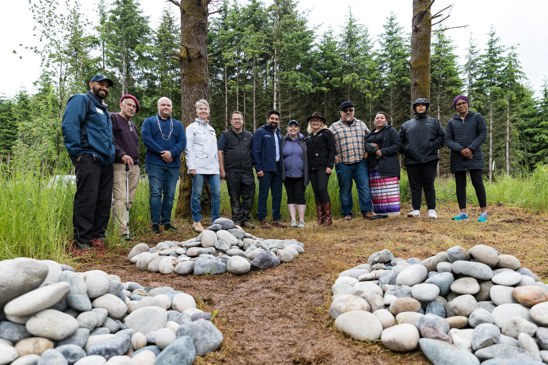 a line of people smiling and standing in a forested park in front of three piles of smooth rocks