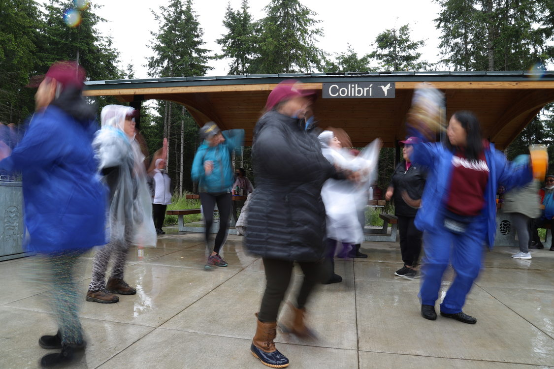 Older people in raingear dancing around a picnic shelter