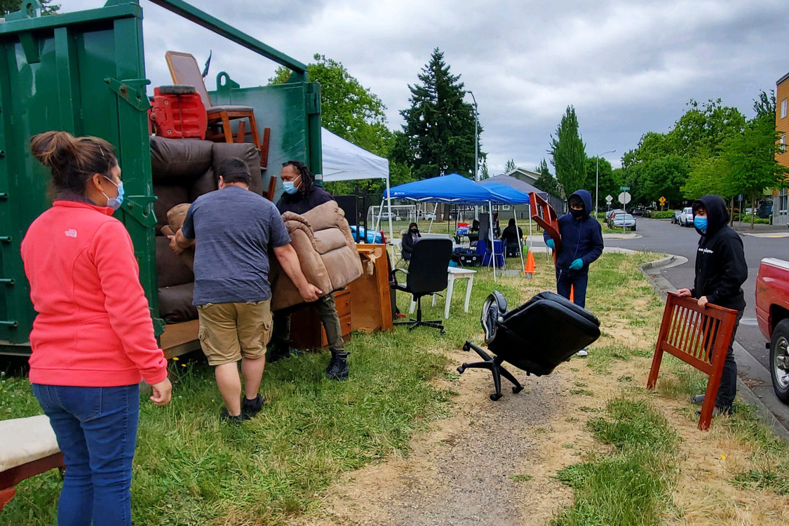 An image of volunteers loading a chair into a dumpster.