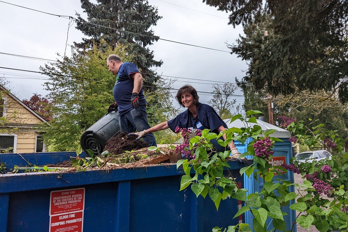 An image of volunteers on top of a dumpster full of yard debris