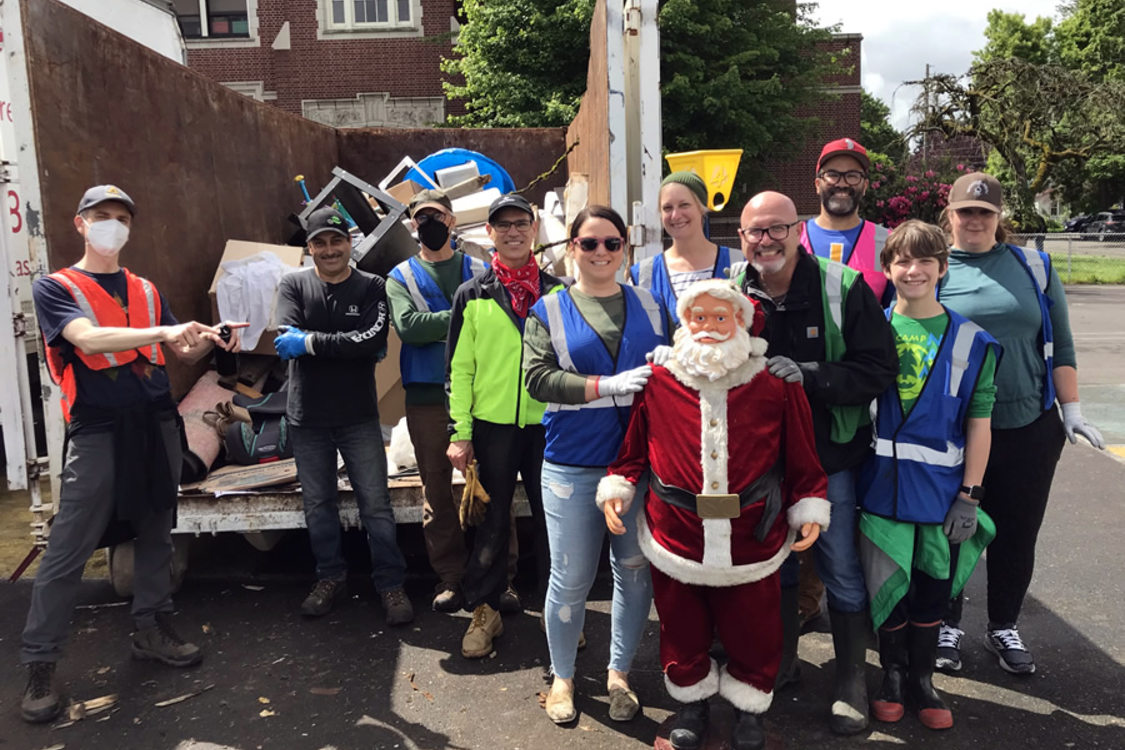 An image of a group of 11 volunteers in front of a dumpster with a plastic santa statue