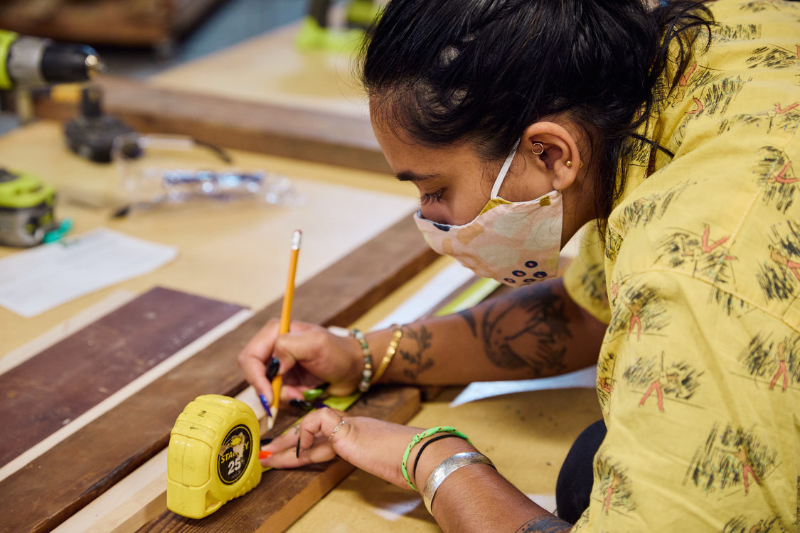 An image of a woman marking a measurement on a piece of wood.