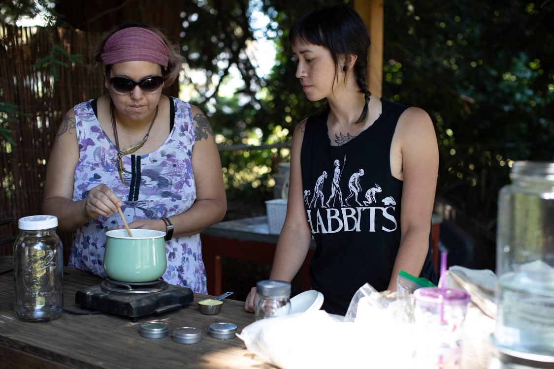 two people who are part of Atabey Medicine Council stand at a wooden table while one of them stirs the plant medicine from the ingredients they gathered earlier