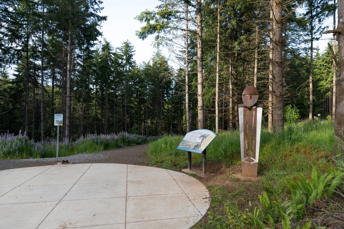 Statue on the right of image welcomes people entering a trail at a nature park.