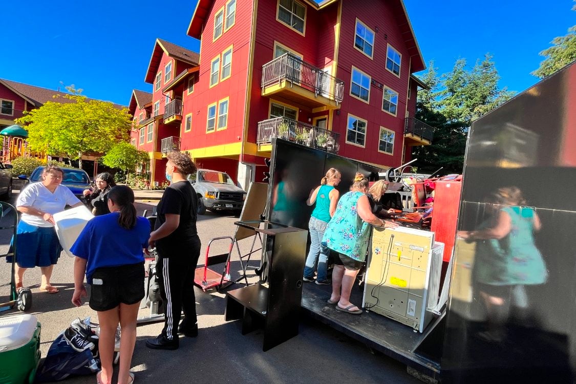 An image of a crowd of people getting rid of pieces of furniture into a truck