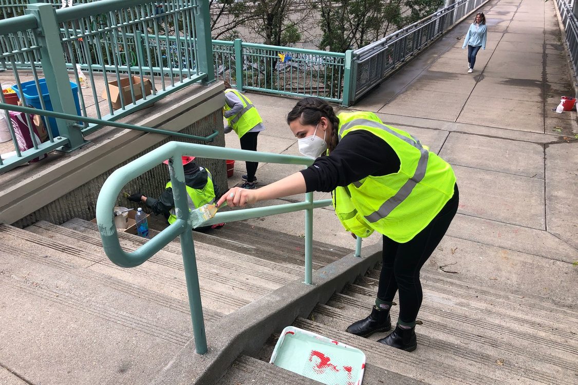 A woman painting a handrail near the Willamette River.
