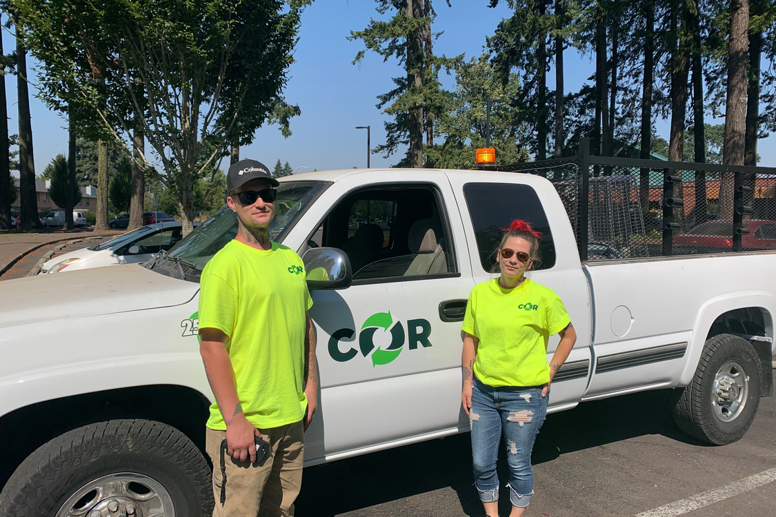 An image of two people in bright neon shirts standing in front of a white pickup truck