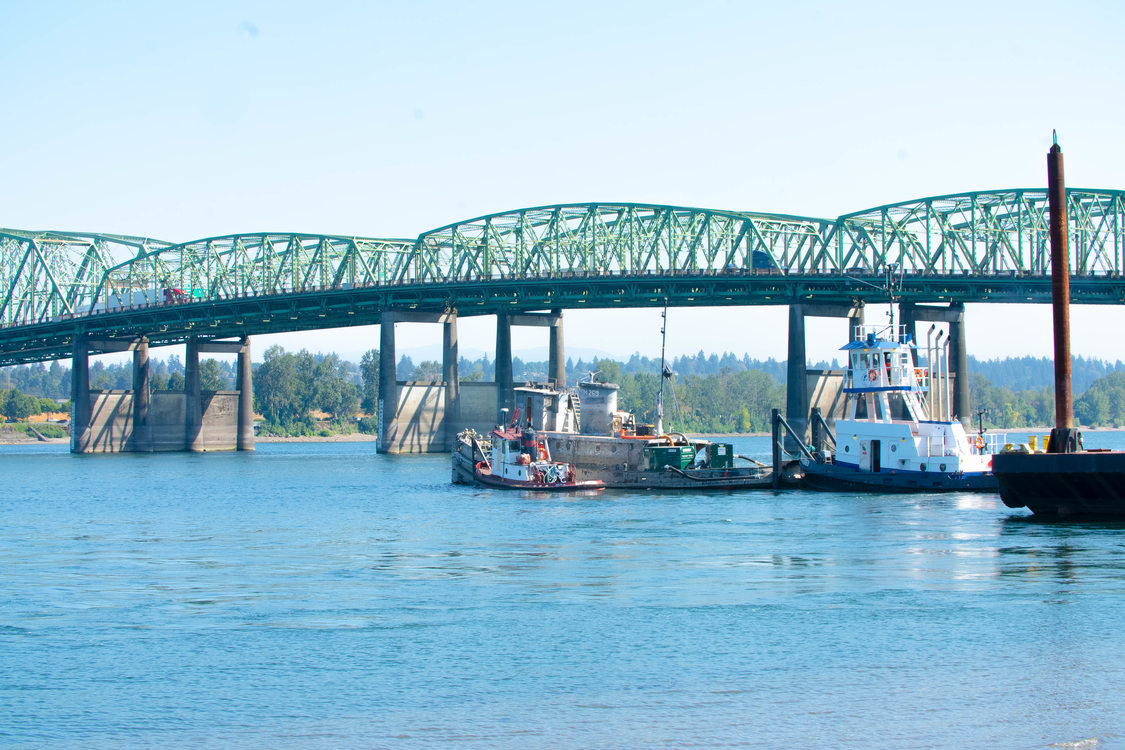 Two tugboats maneuver two derelict boats in the Columbia River, with the Interstate Bridge in the background.