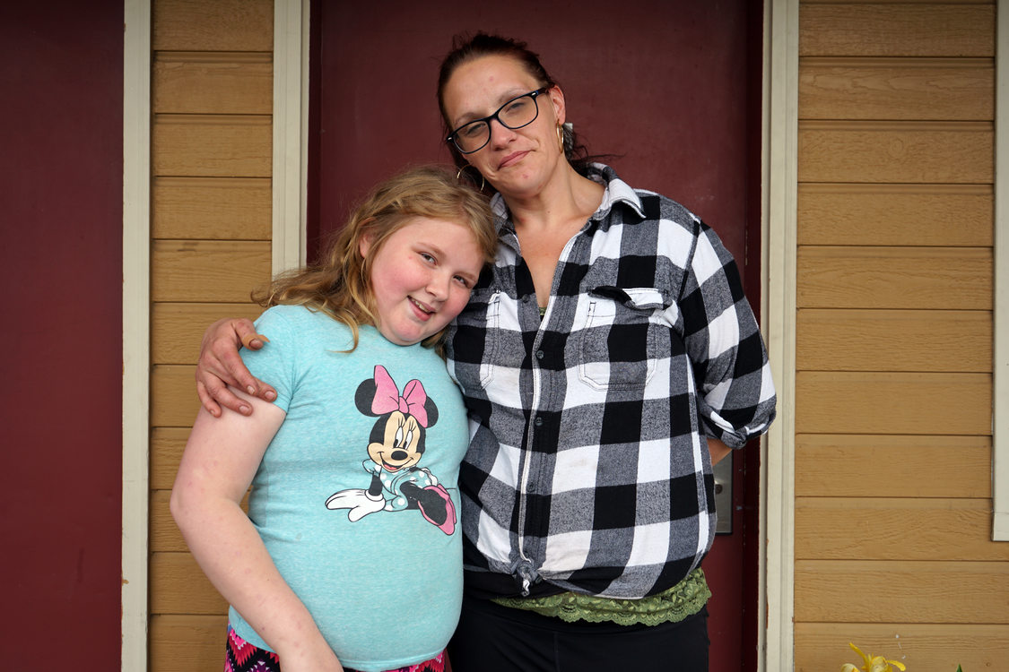Woman in black and white plaid shirt with her arm around a young girl in a blue shirt with Minnie Mouse on it.