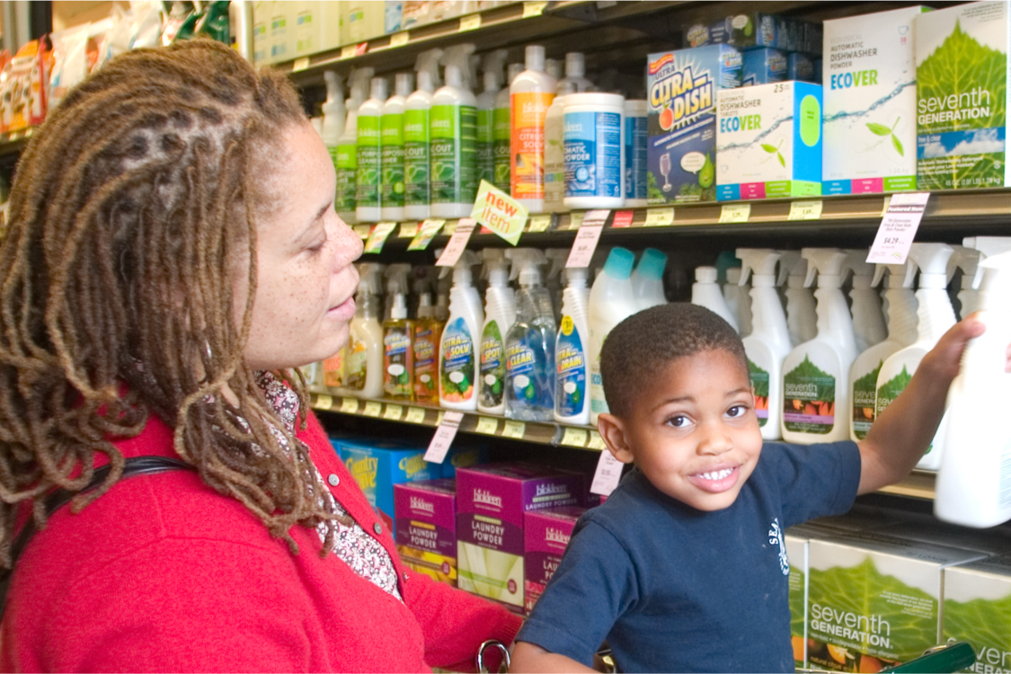 A woman and child are in the cleaning aisle in a grocery store looking at less toxic cleaners