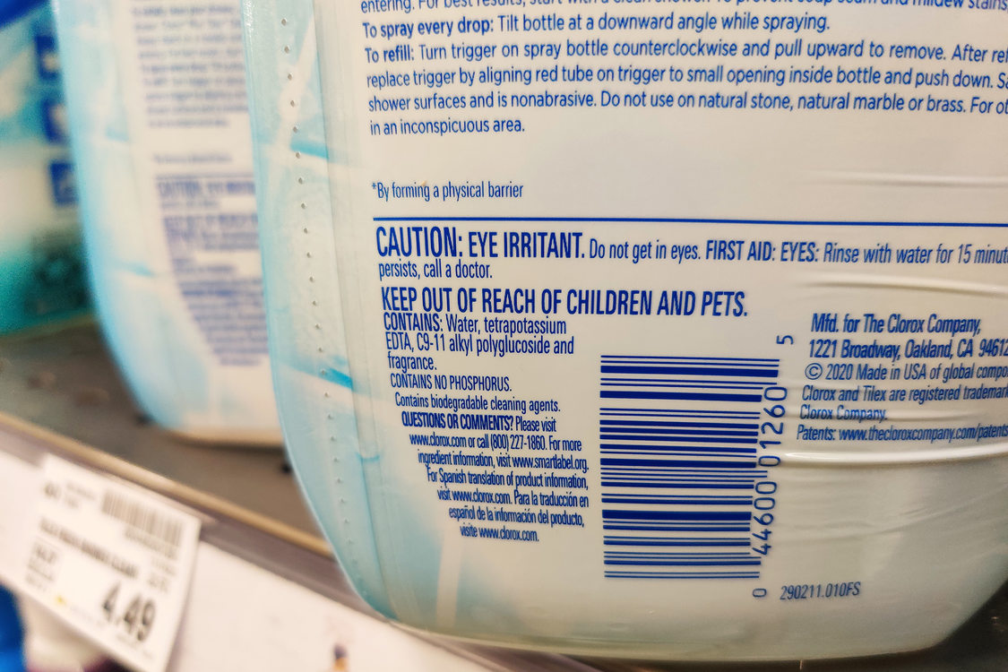 The bottom half of a white bottle of cleaner, the label on the back of the bottle reads caution