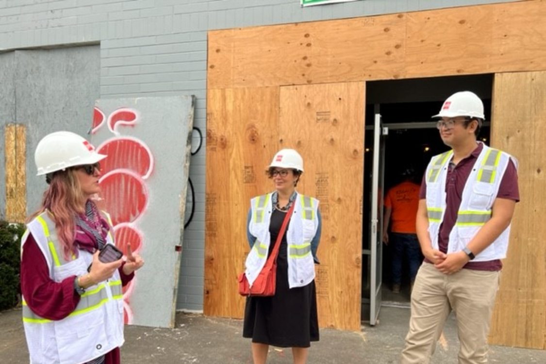 Metro Councilor Duncan Hwang stands next to Jessica Vega Pederson while wearing a white hard hat and safety vest on a construction site visit for Grande Ronde MAT clinic.