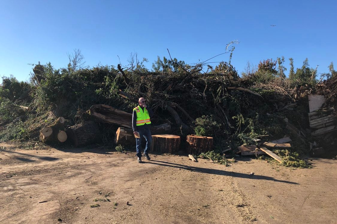 A Metro employee wearing a reflective safety vest stands in front of a large pile of tree debris and waste during an enforcement inspection of a solid waste disposal facility in greater Portland.