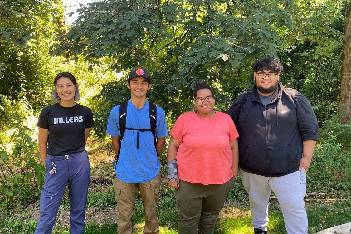 Four youth stand in front of a beautiful forest background