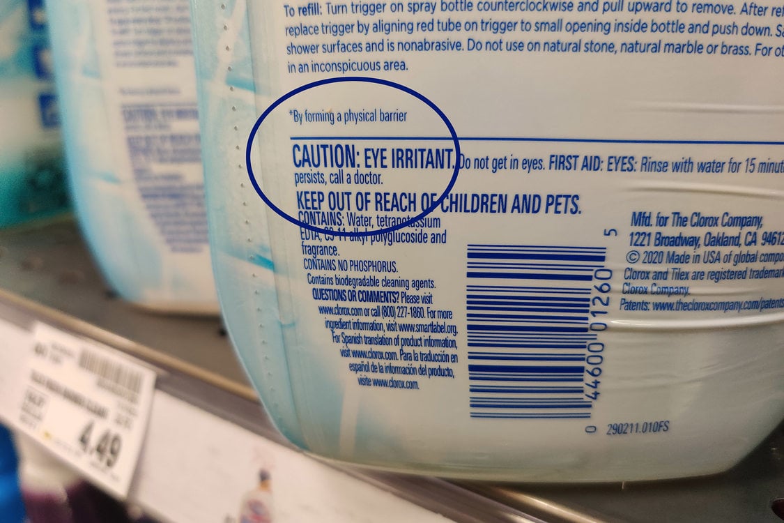 The bottom half of a white bottle of cleaner, the label on the back of the bottle reads caution